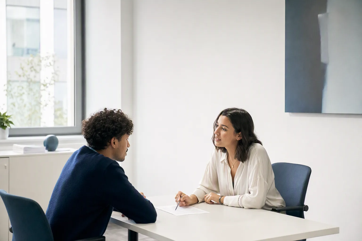 Un étudiant et une recruteuse discutent de part et d'autre d'une table dans un petit bureau, un contrat d'apprentissage posé entre eux